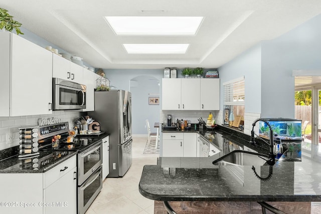 kitchen featuring dark stone counters, decorative backsplash, appliances with stainless steel finishes, a peninsula, and a sink