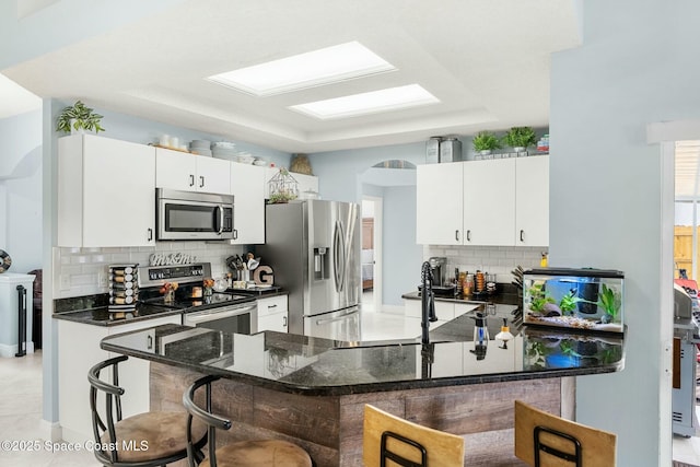 kitchen with a kitchen bar, white cabinets, tasteful backsplash, and stainless steel appliances