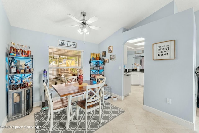 dining area featuring baseboards, vaulted ceiling, light tile patterned flooring, arched walkways, and a ceiling fan