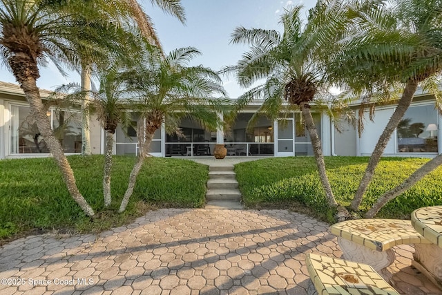 rear view of property with stucco siding, a yard, and a sunroom