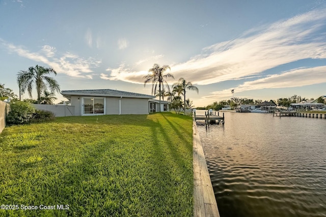 view of dock with a lawn, fence, and a water view