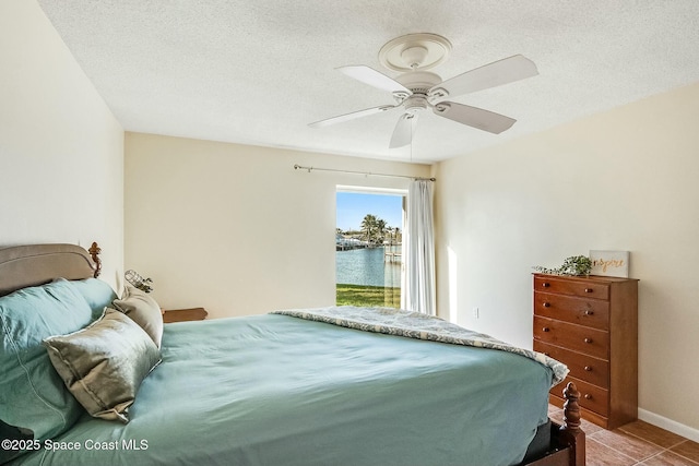 bedroom featuring tile patterned flooring, baseboards, ceiling fan, a water view, and a textured ceiling