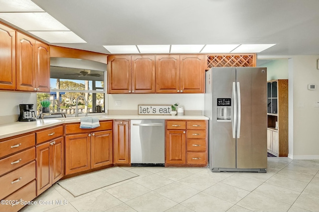 kitchen with a sink, stainless steel appliances, brown cabinetry, light countertops, and ceiling fan