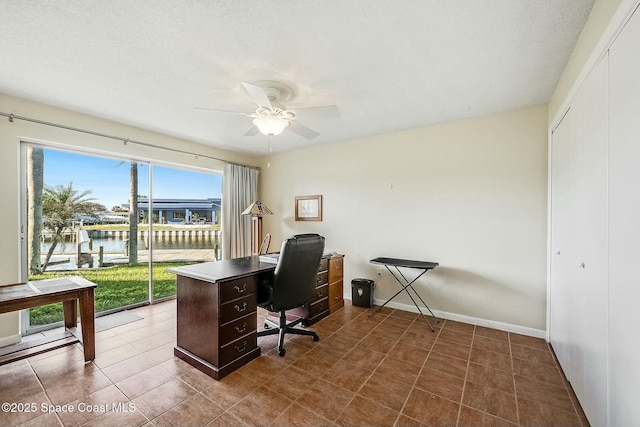 office with dark tile patterned floors, baseboards, a water view, and ceiling fan