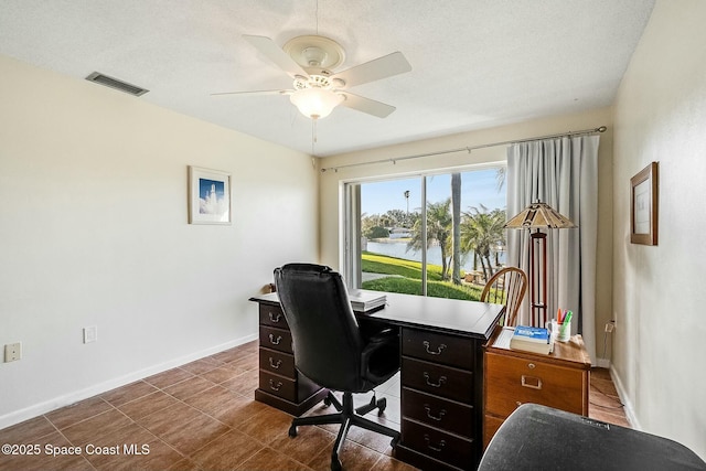 office area featuring visible vents, baseboards, ceiling fan, a water view, and dark tile patterned flooring