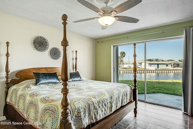 bedroom with a water view, a ceiling fan, a textured ceiling, tile patterned flooring, and access to exterior