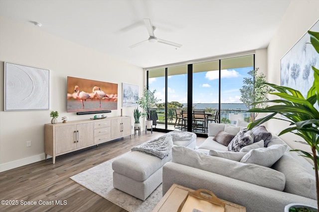 living room with a wall of windows, wood finished floors, baseboards, and ceiling fan