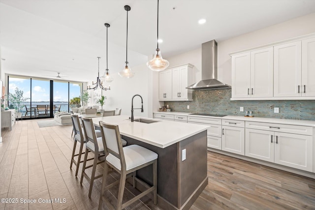 kitchen with a wall of windows, a sink, decorative backsplash, wall chimney range hood, and black electric cooktop