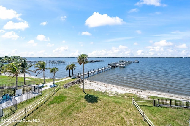 view of dock featuring a water view, a lawn, and fence