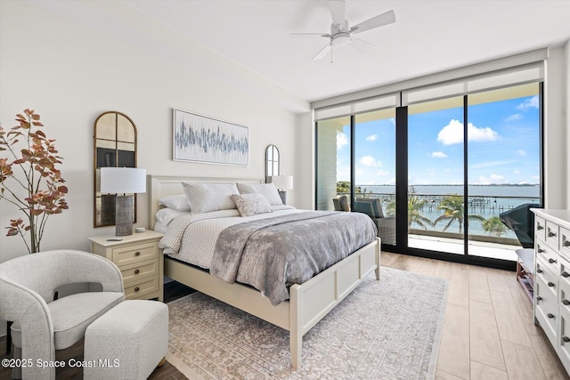 bedroom with a wall of windows, a water view, access to exterior, and a ceiling fan