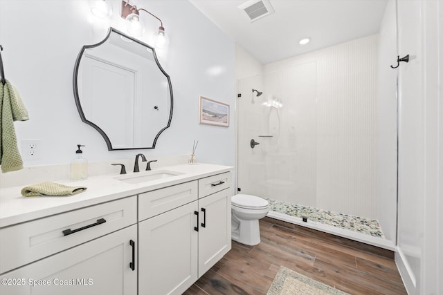 full bath featuring visible vents, toilet, a tile shower, wood finished floors, and vanity