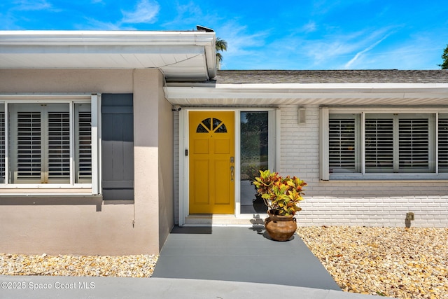 entrance to property with a shingled roof, brick siding, and stucco siding