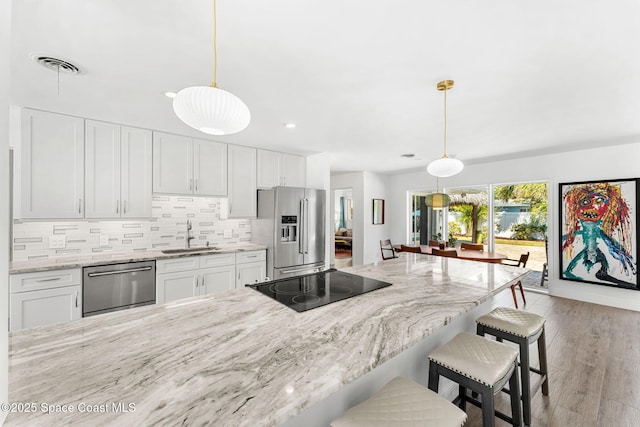 kitchen with visible vents, backsplash, a kitchen bar, stainless steel appliances, and a sink