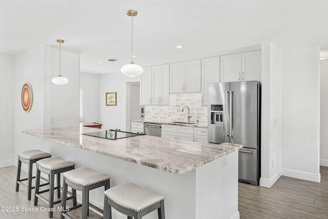 kitchen with a breakfast bar, a sink, decorative backsplash, stainless steel appliances, and white cabinetry