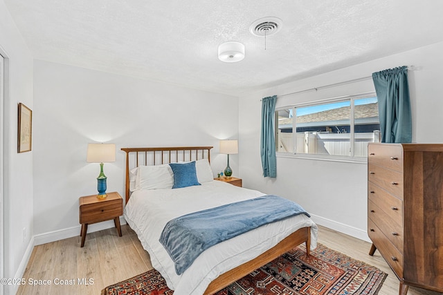 bedroom featuring visible vents, baseboards, a textured ceiling, and light wood-style flooring