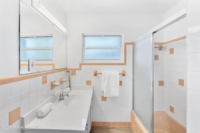 full bathroom featuring a wainscoted wall, vanity, wood finished floors, combined bath / shower with glass door, and tile walls