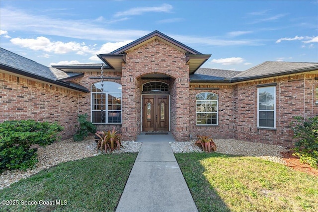 doorway to property with french doors, brick siding, a yard, and a shingled roof