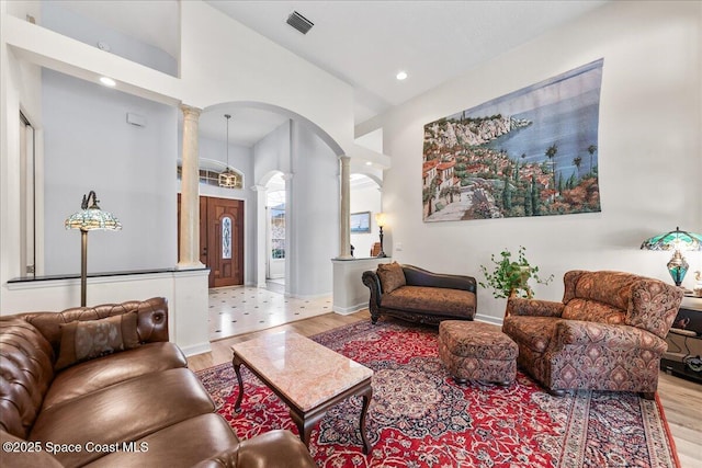 living area with decorative columns, arched walkways, visible vents, and wood finished floors