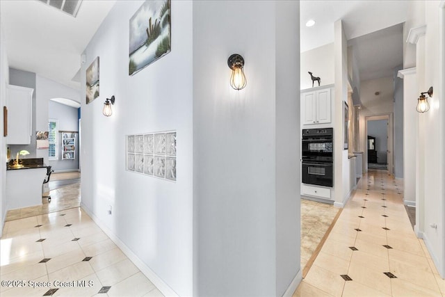 hall featuring light tile patterned floors, visible vents, arched walkways, and baseboards