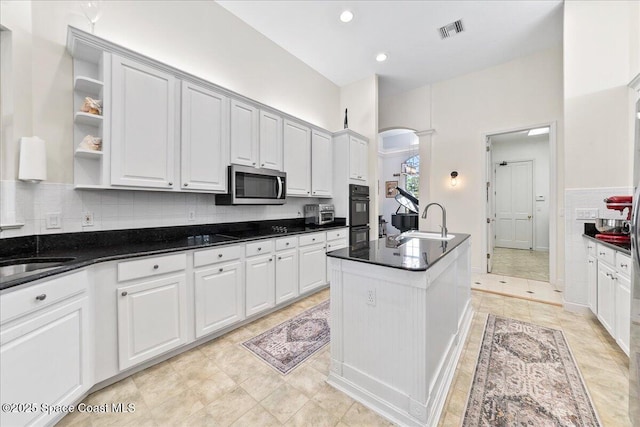 kitchen featuring visible vents, open shelves, a sink, stainless steel microwave, and tasteful backsplash