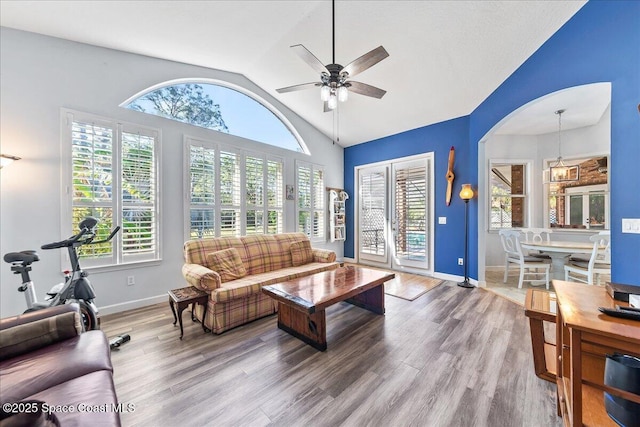 living room with wood finished floors, a ceiling fan, baseboards, high vaulted ceiling, and arched walkways