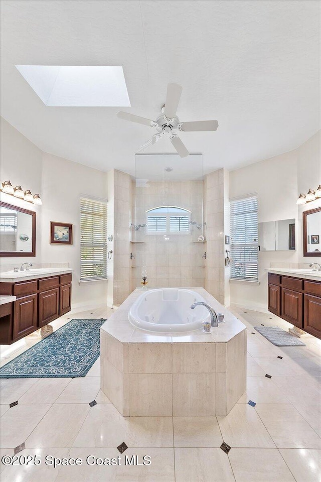 full bathroom featuring a ceiling fan, a skylight, two vanities, tile patterned floors, and a jetted tub