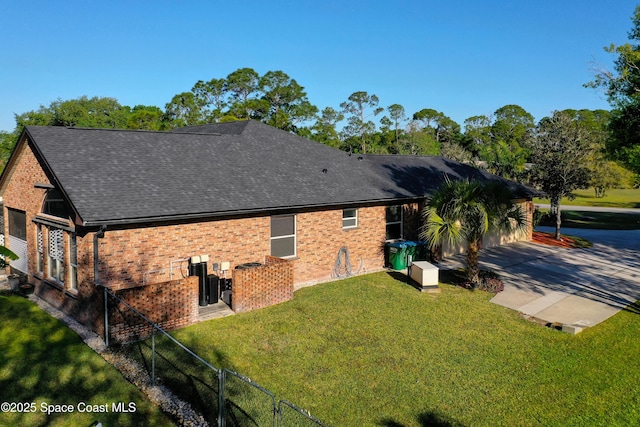 view of property exterior with driveway, fence, a yard, a shingled roof, and brick siding