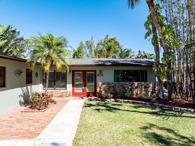 view of front of property with brick siding, stucco siding, french doors, and a front yard