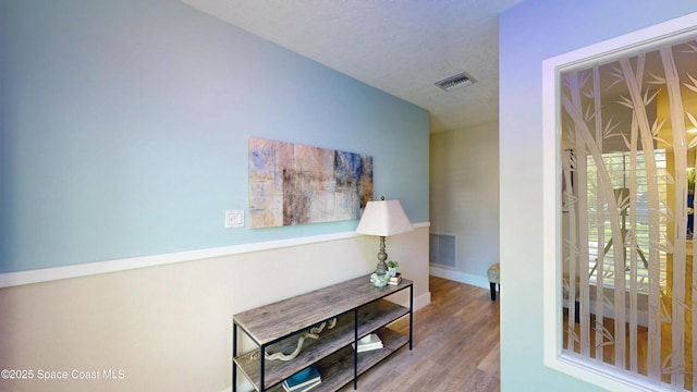 corridor with visible vents, a textured ceiling, baseboards, and wood finished floors