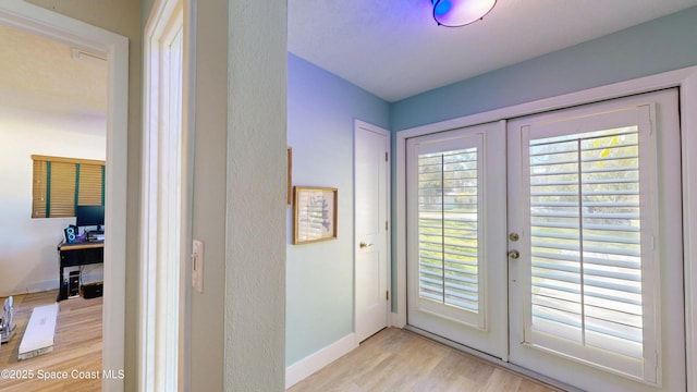 doorway with french doors, light wood-style floors, and baseboards