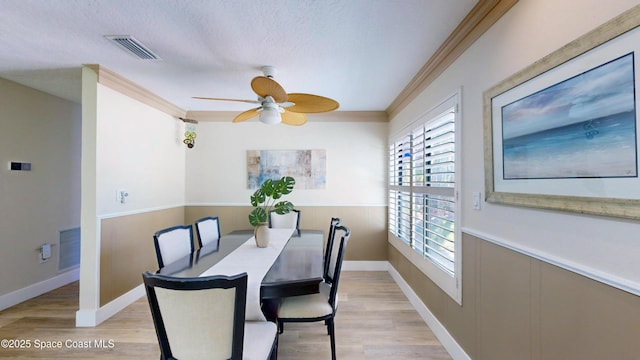 dining space featuring visible vents, a wainscoted wall, light wood-style floors, and ornamental molding