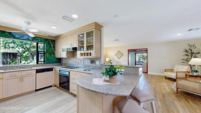 kitchen featuring ventilation hood, a peninsula, a sink, black appliances, and a kitchen breakfast bar