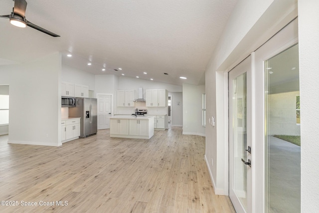 531 Ortega St SE, Palm Bay, FL 32909 - kitchen with open floor plan, white cabinetry, stainless steel appliances, wall chimney range hood, and vaulted ceiling