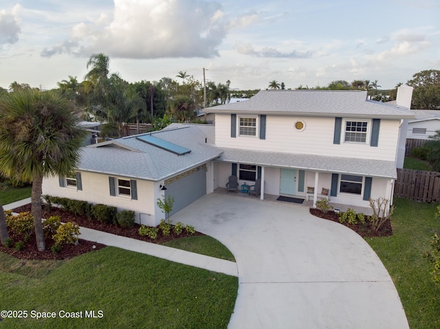 traditional-style home featuring a front lawn, a porch, fence, concrete driveway, and a garage