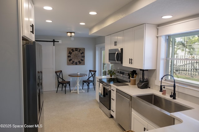 kitchen with a sink, a barn door, white cabinets, and stainless steel appliances