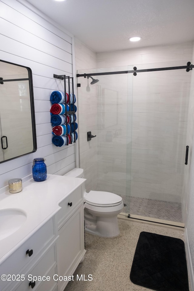 bathroom featuring vanity, speckled floor, a shower stall, wood walls, and toilet