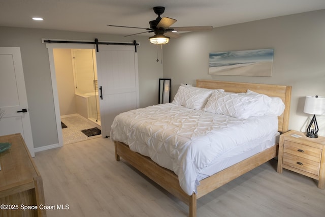 bedroom featuring light wood finished floors, recessed lighting, baseboards, and a barn door