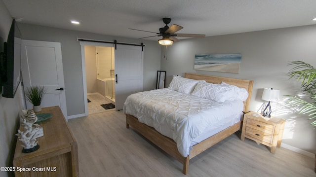 bedroom with light wood-type flooring, a barn door, connected bathroom, baseboards, and ceiling fan