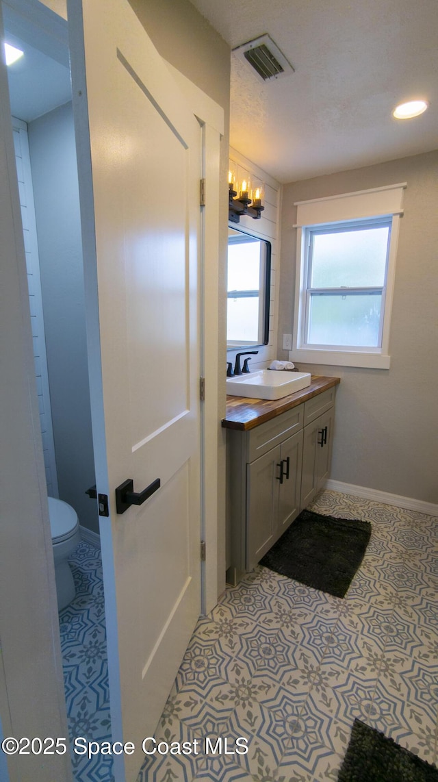 bathroom with vanity, baseboards, visible vents, tile patterned flooring, and toilet