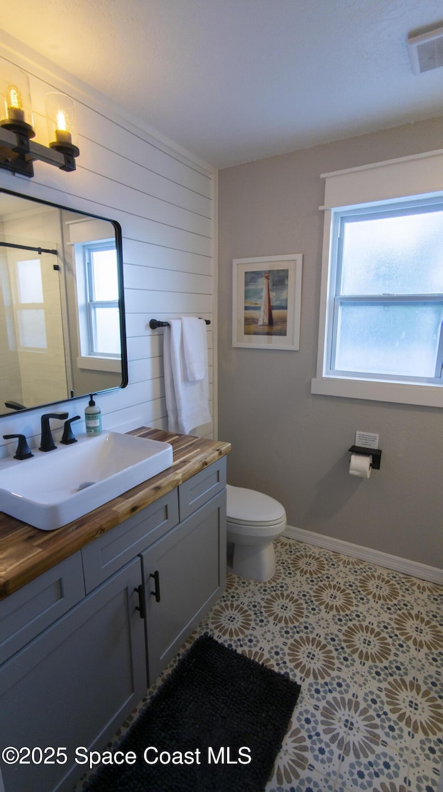 bathroom featuring vanity, baseboards, visible vents, wood walls, and toilet