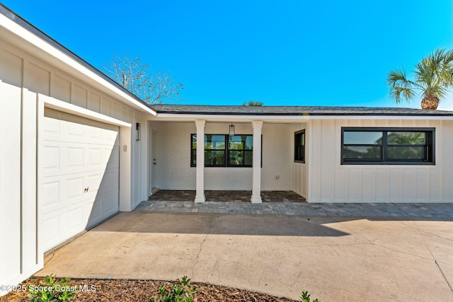 property entrance featuring brick siding, board and batten siding, an attached garage, and driveway