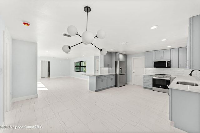 kitchen featuring gray cabinets, a sink, decorative backsplash, stainless steel appliances, and open floor plan