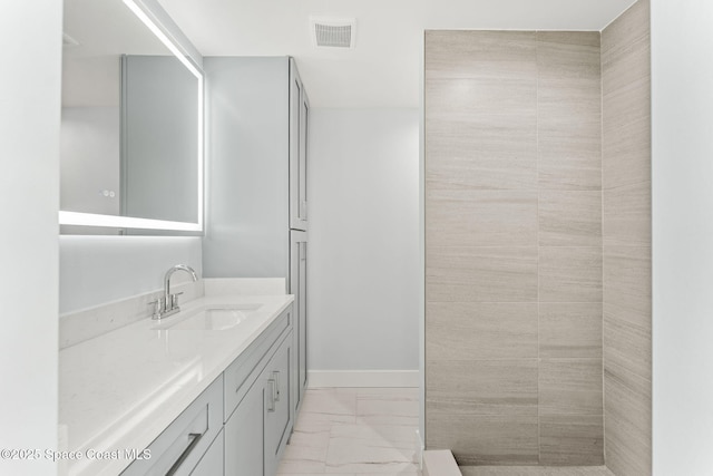 bathroom featuring visible vents, baseboards, a tile shower, marble finish floor, and vanity