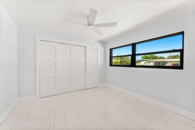 unfurnished bedroom with a closet, baseboards, marble finish floor, and a ceiling fan