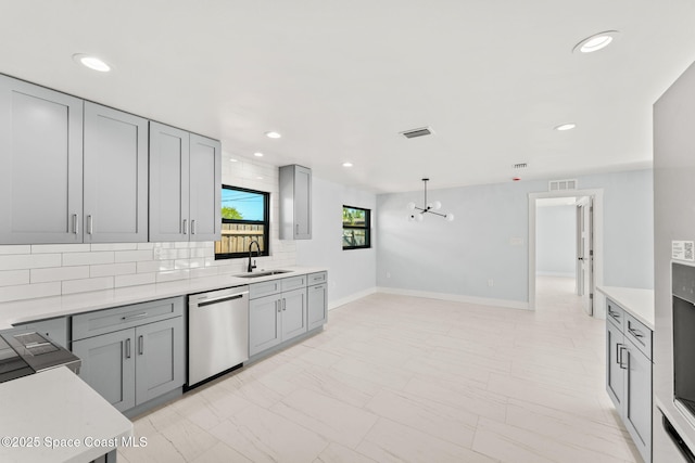 kitchen featuring gray cabinetry, a sink, light countertops, dishwasher, and backsplash