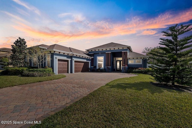 view of front of home featuring decorative driveway, a lawn, a garage, and stucco siding