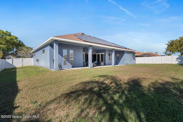 back of property with stucco siding, a lawn, roof mounted solar panels, a fenced backyard, and a patio area