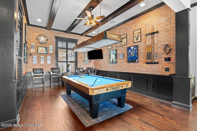 game room featuring brick wall, ceiling fan, beamed ceiling, hardwood / wood-style floors, and wainscoting