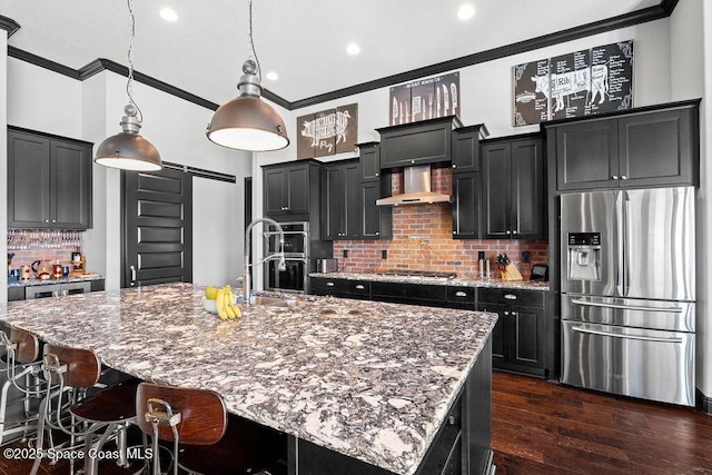 kitchen featuring ornamental molding, stainless steel appliances, a barn door, wall chimney exhaust hood, and dark cabinets