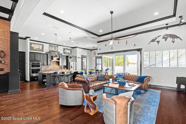 living room with dark wood finished floors, baseboards, a tray ceiling, and ornamental molding